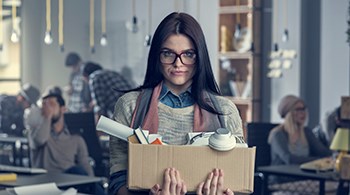 listing-women-carrying-a-box-with-books-and-rolled-up-paper-with people-at-tables-in-background .jpg